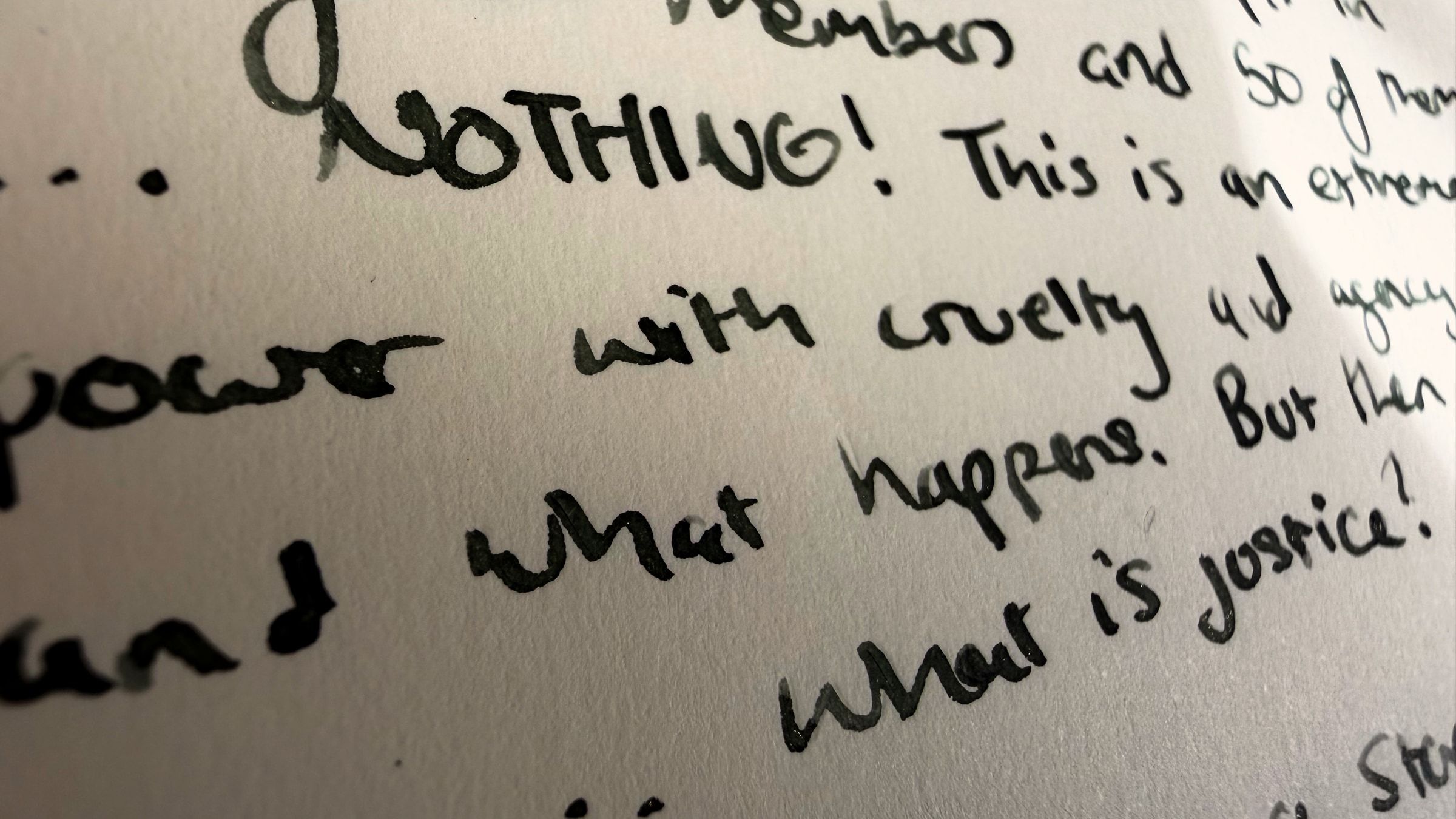 A handwritten notebook page photographed close and at an angle. The word NOTHING, capitalised and followed by an exclamation mark, dominates the frame. Below it, the words with cruelty, what happens, and what is justice.